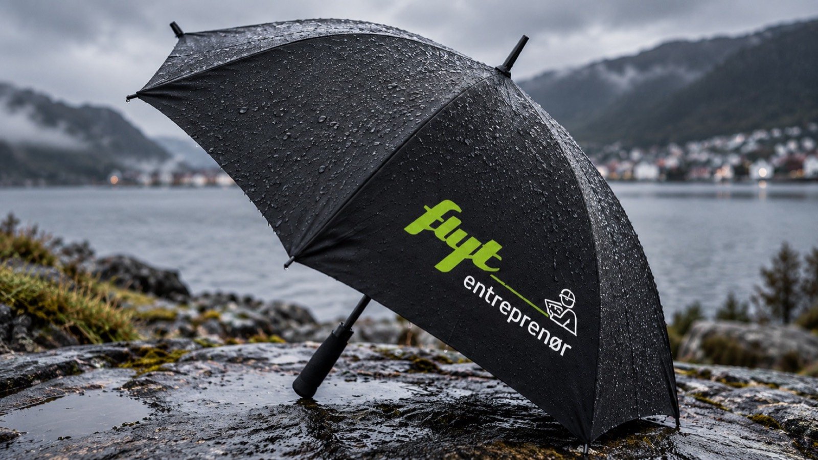 Paraply med Flyt entreprenør-logo i regnvær ved fjorden