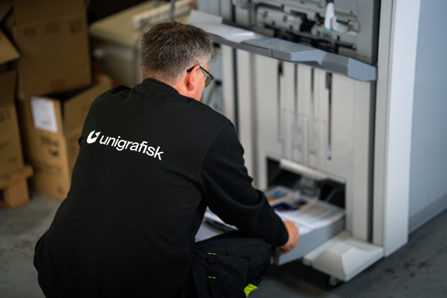Ansatt i svart jakke med Unigrafisk-logo på ryggen